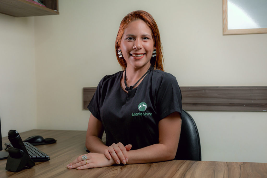Profissional da Monte Verde sentada à mesa de atendimento, com uniforme da empresa.