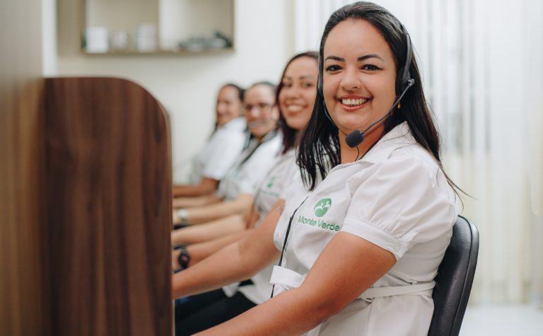 Atendente da Monte Verde com headset no escritório, com a equipe ao fundo.