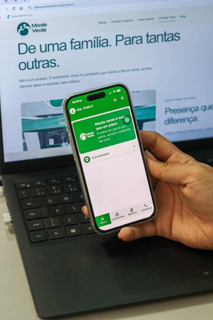 Celular exibindo o aplicativo Monte Verde, com acesso a carteirinha, boletos e contatos.