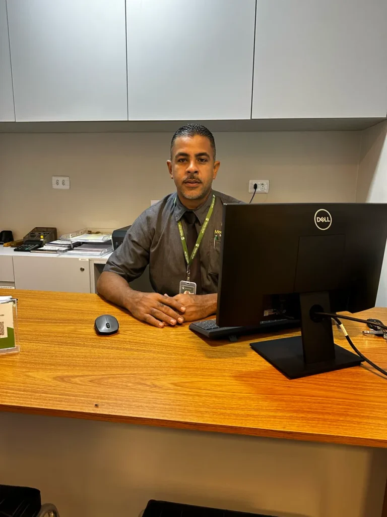 Profissional da Monte Verde sentado à mesa de atendimento, ao lado de um monitor.