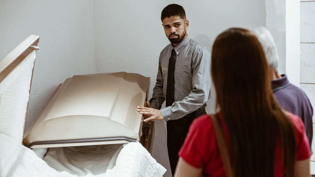 Profissional apresenta uma urna funerária a duas pessoas.
